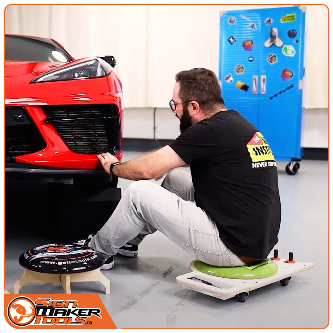 Signmaker using the LowRider seat to apply graphics on a red car bumper