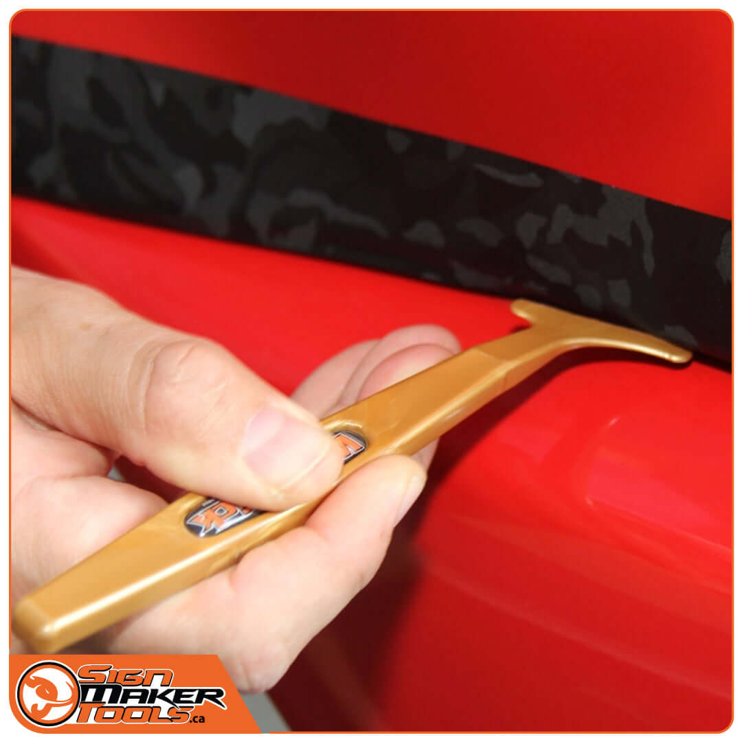 Hand using WrapStick Flex Gold to tuck vinyl along vehicle trim
