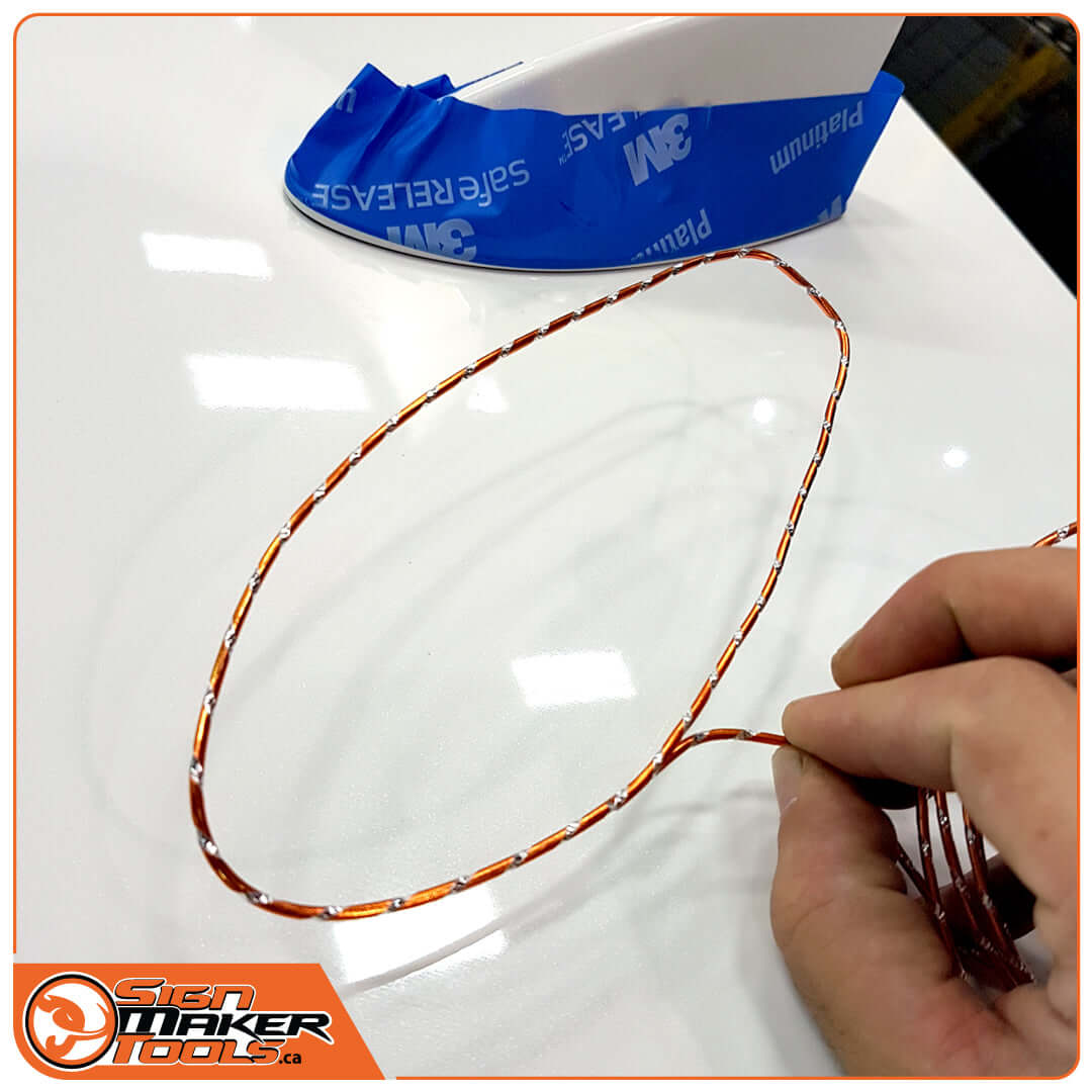 Hand shaping WrapBend-it wire to outline the contour of a vehicle's fin on a white surface