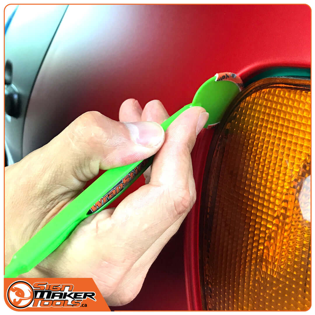 Hand using WrapStick Betty tool on car's headlight edge for vinyl installation