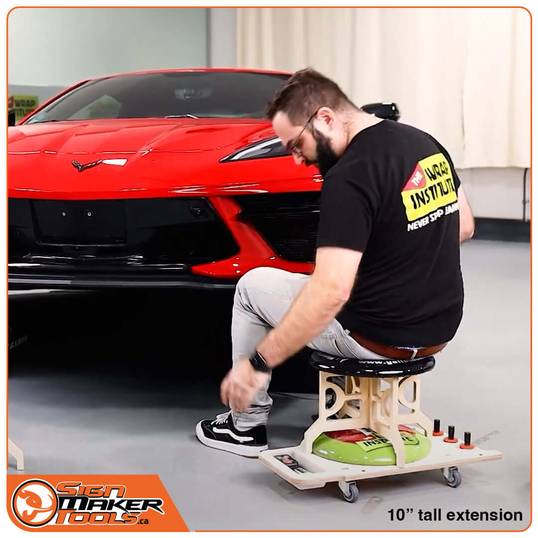 Signmaker seated on LowRider 10-inch extension applying wrap to a red car