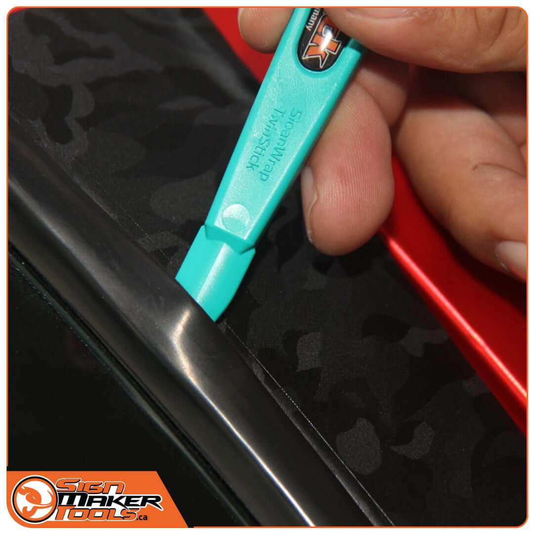 Angled end of WrapStick Sloan being used to lift car window seal on a wrapped vehicle