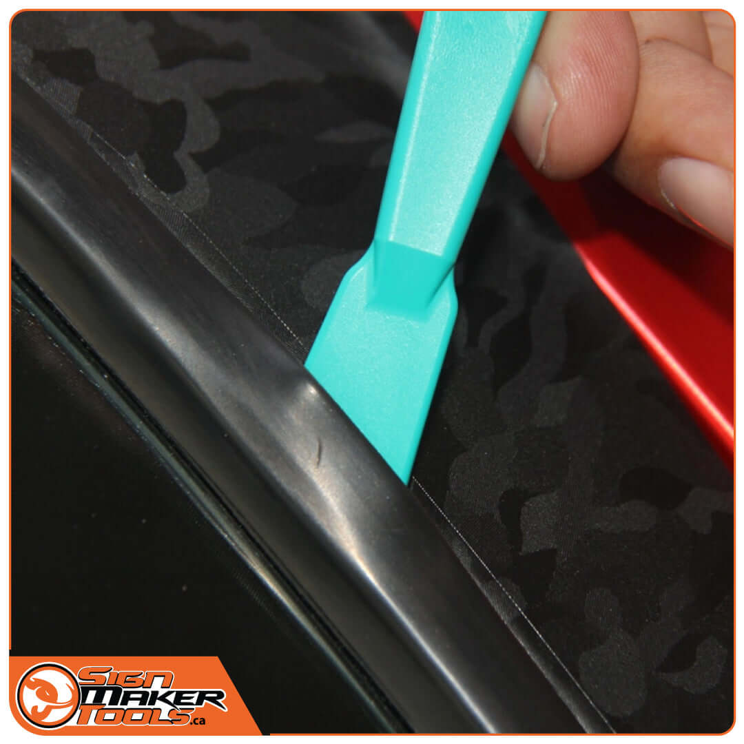 WrapStick tool lifting seal and smoothing vinyl along car edge