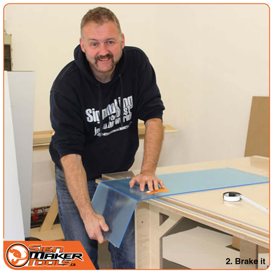 Man breaking a scored plexiglass sheet with his hands during the cutting process
