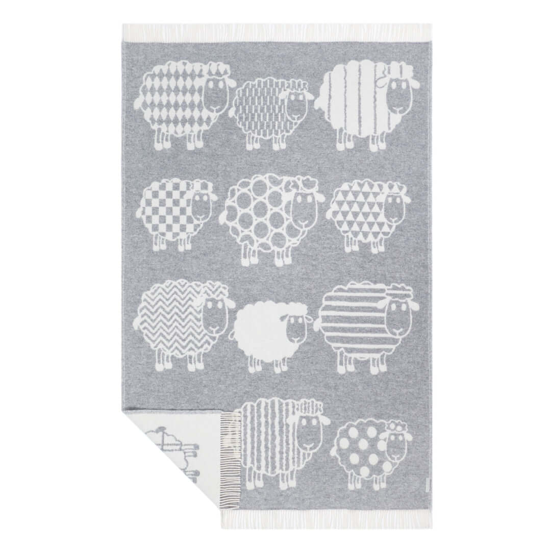 Flat lay of a grey wool throw blanket featuring playful white sheep designs with various patterns