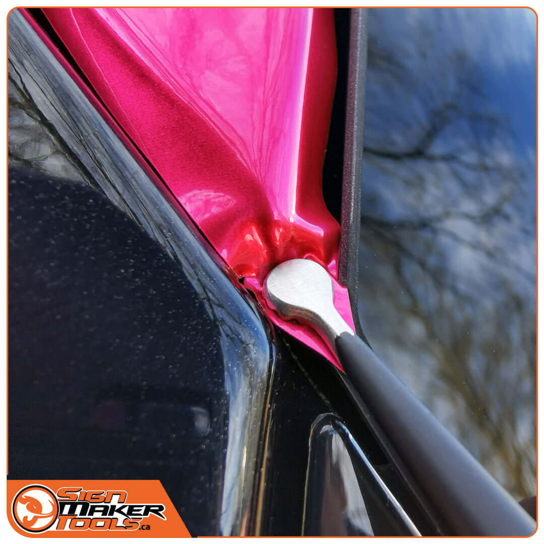 WrapTweezer Disc tweezers stretching pink wrap film over a car edge for smooth application